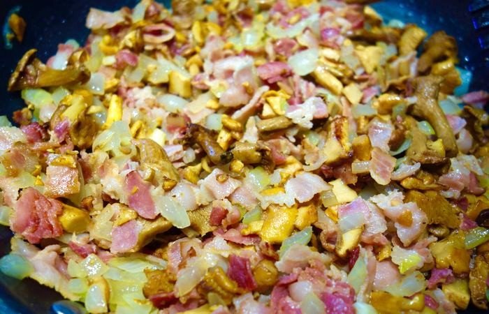 Blandning av stekt svamp och bacon i en svart stekpanna.